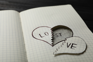 Photo of Broken heart with words LOVE and LOST in notebook on table, closeup. Relationship problems concept