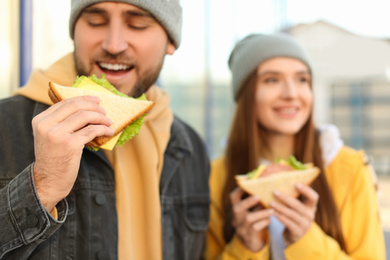 Photo of Happy young couple with sandwiches on city street