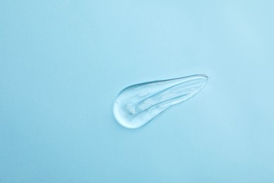 Smear of transparent ointment on light blue background, top view