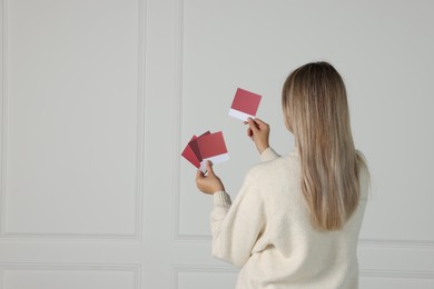 Photo of Woman with color sample cards choosing paint shade for wall indoors, back view. Interior design