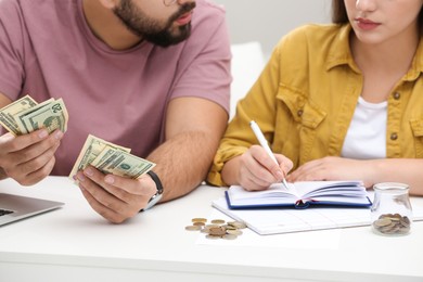 Young couple counting money at white table indoors, closeup