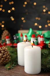 Photo of Burning candles and festive decor on wooden table against blurred Christmas lights