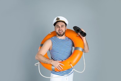 Happy sailor with binoculars and ring buoy on light grey background