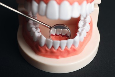 Photo of Jaw model and dental mirror on black background, closeup. Gum inflammation