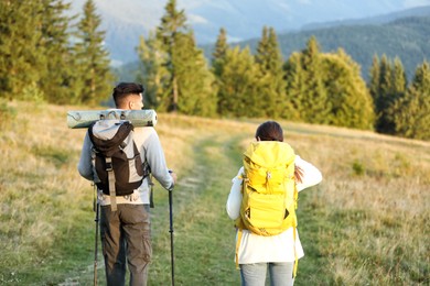 Photo of Couple with backpacks and trekking poles hiking in mountains, back view. Tourism equipment