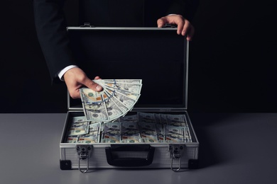 Businessman with suitcase full of money on dark background