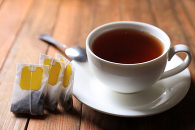 Photo of Tea bags near cup of hot drink on wooden table, closeup