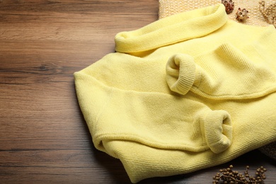 Photo of Yellow warm sweater with plaid on wooden table, closeup. Space for text