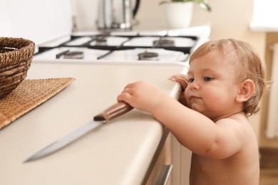 Little child holding sharp knife in kitchen. Dangerous situation