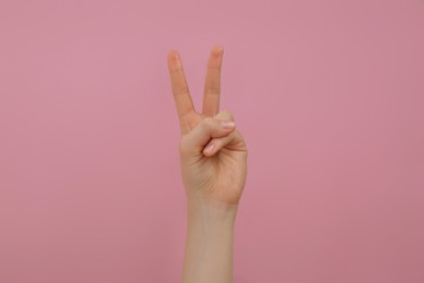 Woman showing two fingers on pink background, closeup