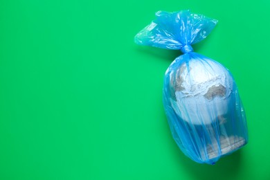 Photo of Globe in plastic bag and space for text on light green background, top view. Environmental conservation