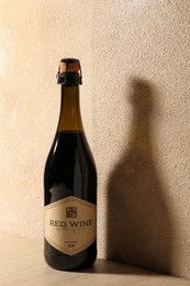 Photo of Bottle of tasty red wine on wooden table near beige wall