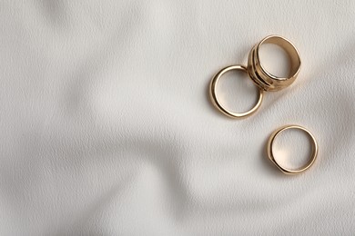 Elegant golden rings on white fabric, flat lay with space for text. Stylish bijouterie
