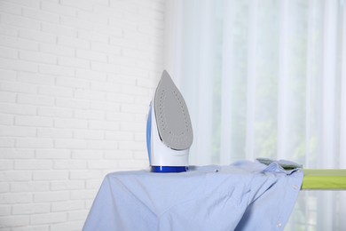 Photo of Modern iron and clean shirt on board indoors