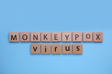 Photo of Words Monkeypox Virus made of wooden cubes on light blue background, top view