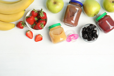Jars with baby food and fresh ingredients on white wooden table, flat lay. Space for text