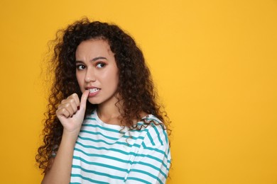Photo of African-American woman biting her nails on yellow background. Space for text