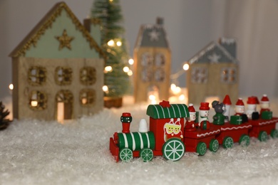 Bright toy train near decorative houses with Christmas lights on artificial snow