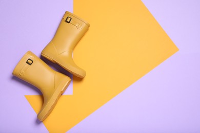 Pair of yellow rubber boots on color background, top view. Space for text