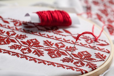 White fabric with red Ukrainian national embroidery in hoop, needle and thread, closeup