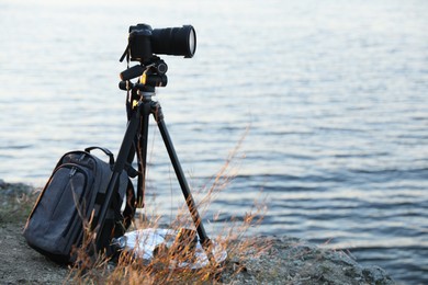 Tripod with modern camera and set of photography equipment on rocky river coast. Space for text
