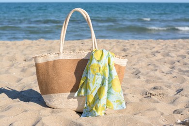 Photo of Straw bag with beach wrap on sandy seashore. Summer accessories
