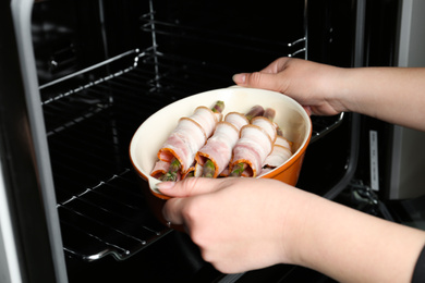 Woman putting ceramic baking dish with bacon wrapped asparagus in oven, closeup