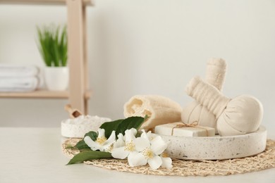 Beautiful jasmine flowers, herbal bags and soap bar on white wooden table indoors, space for text