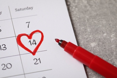 Calendar with marked Valentine's Day and red felt tip pen on grey table, closeup