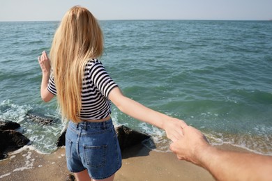 Photo of Young woman holding boyfriend's hand near sea on sunny day in summer