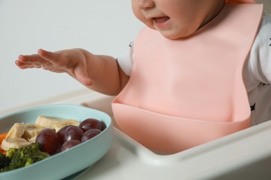 Cute little baby wearing bib while eating on white background, closeup
