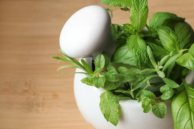 Photo of Mortar with different fresh herbs on wooden table, closeup. Space for text