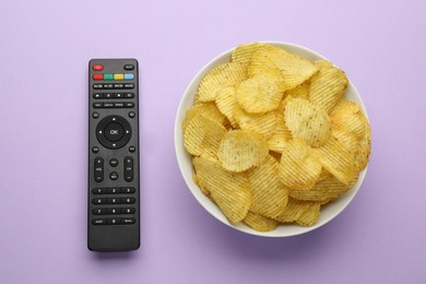 Remote control and bowl of potato chips on violet background, flat lay