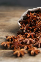 Overturned bag with aromatic anise stars on wooden table, closeup