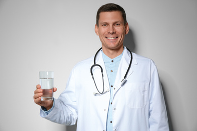 Nutritionist holding glass of pure water on light grey background
