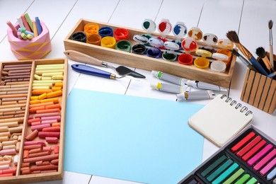 Blank sheet of paper, colorful chalk pastels and other drawing tools on white wooden table. Modern artist's workplace