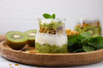 Photo of Delicious dessert with kiwi, yogurt and muesli on wooden board, closeup