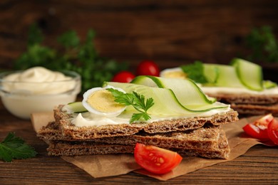 Fresh rye crispbreads with quail egg, cream cheese and cucumber slices on wooden table, closeup