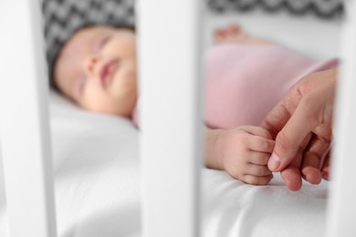 Photo of Mother holding hand of her baby in crib, closeup