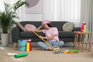 Tired young woman sitting on floor and cleaning supplies in living room