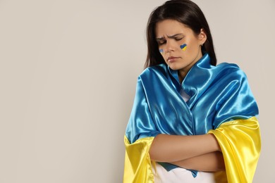 Photo of Sad young woman with face paint and Ukrainian flag on beige background, space for text