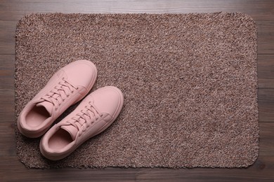 New clean door mat with shoes on wooden floor, above view