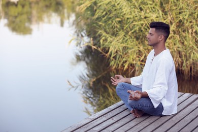 Man meditating on wooden pier near river. Space for text