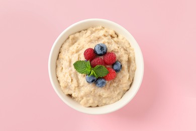 Tasty oatmeal porridge with raspberries and blueberries in bowl on pink background, top view
