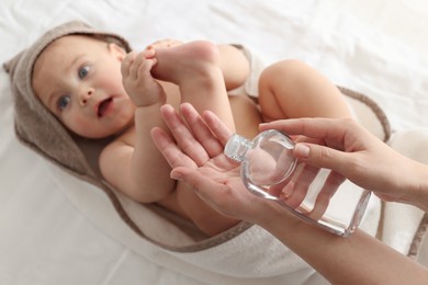 Mother with bottle of massage oil near baby on bed, closeup