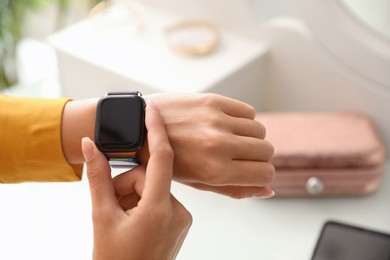 Woman checking stylish smart watch at home, closeup