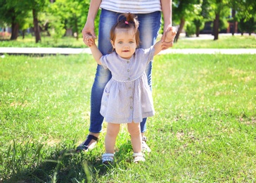 Adorable baby girl holding mother's hands while learning to walk outdoors