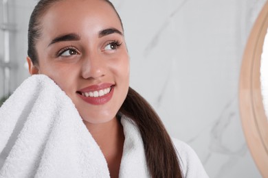 Beautiful young woman wiping face with towel in bathroom, closeup. Facial wash