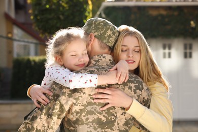 Photo of Daughter and wife hugging soldier in Ukrainian military uniform outdoors. Family reunion