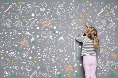 Little child drawing with colorful chalk on gray wall